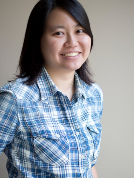 Yihwen Chen, Portrait. A person with brown eyes and shoulder-long black hair smiles into the camera. She wears a blue and white checked shirt.